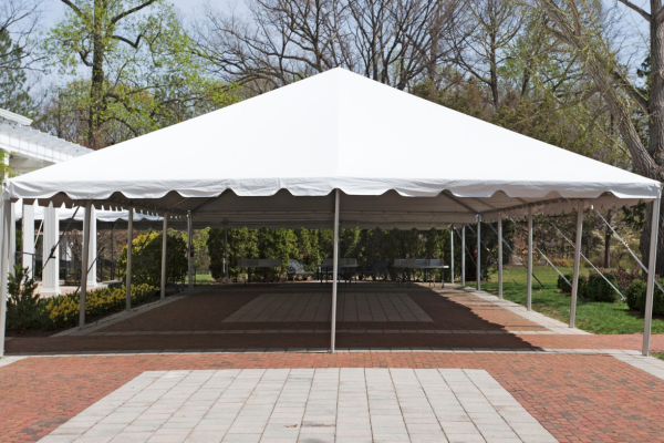 White tent set up outdoors on a brick patio with trees in the background